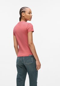 Kortermet, tettsittende t-skjorte i myk korallfarge, med rund hals og logomerke ved sømmen, kombinert med høyhalsede denimjeans.