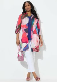 Kolorowy, długi płaszcz z kwiatowym wzorem, krótkie rękawy, noszony na niebieskim topie, w zestawie z białymi spodniami, różową torbą i pasującymi sandałami.