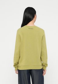 Ελαιοπράσινη μπλούζα με στρογγυλή λαιμόκοψη, ραμμένα μανίκια και στρίφωμα. Διαθέτει διακριτική σήμανση σε μαύρο χρώμα στο επάνω μέρος της πλάτης. Μαλακή υφή.