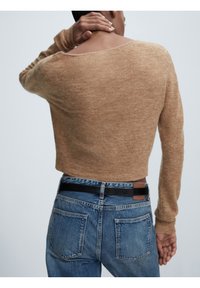 Gestrickter, kurz geschnittener Pullover in Hellbraun mit langen Ärmeln und weitem Ausschnitt, kombiniert mit blauen Denim-Jeans mit schwarzem Gürtel.
