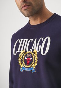 Sudadera de color navy con "CHICAGO" en grandes letras bordadas en blanco, que presenta un emblema de cabeza de toro colorido y acentos dorados de laurel.