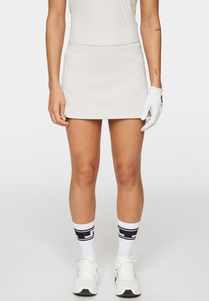 Gonna da golf beige chiaro con una cintura larga, abbinata a scarpe da ginnastica bianche e calze alte fino al ginocchio a righe bianche e nere.