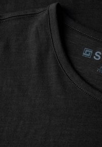 Camiseta de algodón negra con cuello redondo, textura suave y costuras bien acabadas. Etiqueta de la marca visible en el interior del cuello.