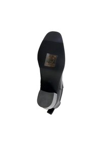 Semelle de chaussure noire avec une surface en caoutchouc lisse, talon texturé pour une meilleure adhérence et un autocollant clair affichant les instructions d'entretien.