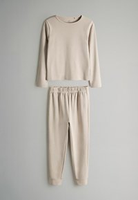 Beige Langarmoberteil mit rundem Halsausschnitt, kombiniert mit passenden elastischen Hosen. Glatte Textur, schmale Bündchen und minimalistisches Design.