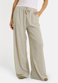 Mujer vistiendo pantalones de pierna ancha a rayas verticales en beige y blanco con cintura ajustable y bolsillos, combinados con una blusa sin mangas blanca.