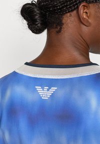 Blå gradient sports skjorte med rund hals, med en hvit logo på baksiden, glatt tekstur og kontrastfarget krage.