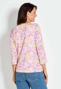 Multikleurige bloemenblouse met driekwart mouwen, met roze, gele en paarse patronen op een lichte achtergrond. Zachte stof.