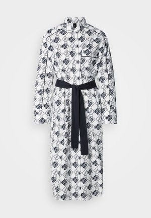 Robe blanche avec un motif géométrique noir, manches longues, patte de boutonnage et une ceinture sombre assortie à la taille.