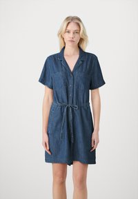 Jeanskjole med korte ermer, knappelukking foran, to brystlommer, innsvingt midje og lengde over kneet i mørkeblå farge.