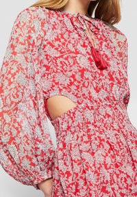 Vestito floreale rosso con motivo paisley bianco, tessuto trasparente, maniche lunghe a sbuffo, scollo a goccia con dettaglio a nappina e inserti laterali.