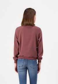 Bordeaux langermet topp med rund hals og elastiske mansjetter, satt sammen med lyseblå fitted jeans, sett fra baksiden.
