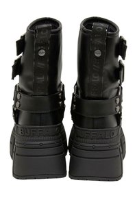 Schwarze Lederstiefeletten mit einer massiven Sohle, verstellbaren Riemen, auffälligen Logo-Details und strukturierten Akzenten an der Ferse.