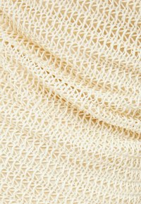 Texturovaná látka v světle béžové barvě s geometrickým krajkovým vzorem. Povrch vypadá jemně a ohebný, ukazuje složité, otevřené tkaniny detaily.