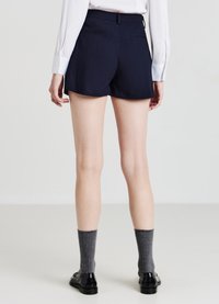 Pantaloni corti navy a righe con orlo svasato, dotati di una cintura in vita e due tasche posteriori. Abbinati a calze grigie a coste e scarpe nere.