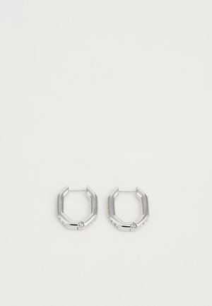 Ett par silverfärgade geometriska hoopsörhängen med hexagonal form och små inlagda kristaller längs kanterna, mot en neutral ljus bakgrund.