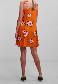 Floral dress with orange fabric, featuring pink and green flower patterns, thin shoulder ties, and a relaxed fit. Green heeled sandals.