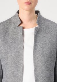 Chaqueta de mezcla de lana gris con un alto cuello, frente abierto y acabado texturizado, superpuesta sobre una camiseta blanca de cuello redondo.