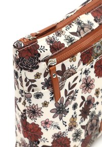 Bolso de tela con estampado floral sobre un fondo cremoso, con dos cierres de cremallera marrón y un detalle en cuero texturizado. Cuenta con múltiples bolsillos.