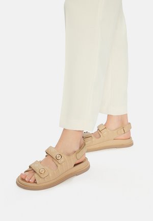 Béžové sandály s nastavitelnými suchými zipy, prošívanou texturou a polstrovanou podrážkou. Pryžová podrážka pro lepší přilnavost.