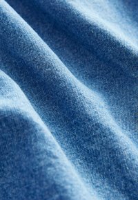 Tissu bleu clair avec une texture lisse, présentant un motif de tissage subtil. L'image capture la douce ondulation et la brillance du matériau.