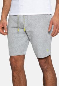 Grå sweatshorts lavet af blødt stof med snor i livet, der har gule detaljer og et lille logo på det nedre venstre ben.