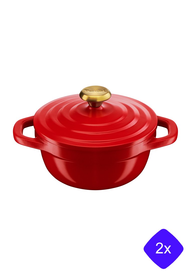 Cocotte en fonte rouge avec un couvercle cannelé et un bouton doré, deux poignées sur les côtés, isolée sur fond blanc.