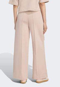 Svetloružové široké nohavice s hladkou textúrou, so bočnými švami a vysokým pásom. V páre s svetlými topánkami pre kontrast.