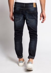 Jeans blu scuro con vestibilità slim, texture sfumata e orli arrotolati. Presentano due tasche posteriori e una patch in pelle beige con il logo in vita.