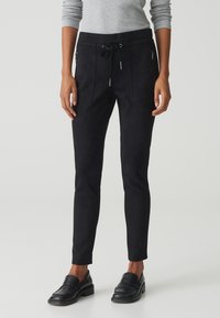 Pantalon de jogging en suède noir avec une taille élastique à cordon, des poches zippées et une coupe slim. Associé à des mocassins noirs.