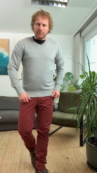 Šedý vlněný svetr s dlouhými rukávy, kombinovaný s úzkými vínovými kalhotami. V pozadí jsou vidět neformální obuv a vnitřní rostliny.