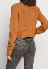 Suéter de punto naranja recortado con dobladillo acanalado y mangas largas, combinado con jeans de tiro alto grises que tienen bolsillos traseros en forma de corazón.