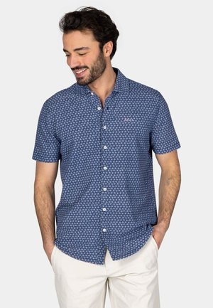 Korte mouwen blauwe shirt met een wit bloemenpatroon, knoopsluiting kraag, en een roze accentknop, gedragen met lichtgekleurde broek.