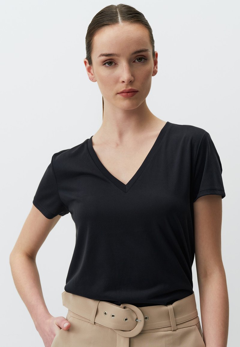 Czarny t-shirt z dekoltem w serek, wykonany z miękkiego, gładkiego materiału, z krótkimi rękawami, w połączeniu z beżowymi spodniami z paskiem z okrągłą klamrą.