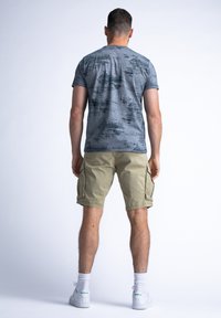 Šedé vzorované tričko a béžové cargo šortky. Tričko má mramorový design. Model nosí bílé tenisky se zelenými akcenty a kotníkové ponožky.