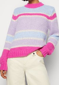 Stickad tröja med rund rosa halsringning, prydd med horisontella ränder i lavendel, blå, vit och stark rosa. Avslappnad passform, texturerad tyg.