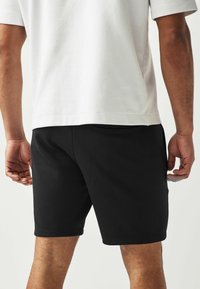 Zwarte korte broek van een katoenmix, kuitlengte, met een platte tailleband en zijzakken, gecombineerd met een witte T-shirt met korte mouwen.