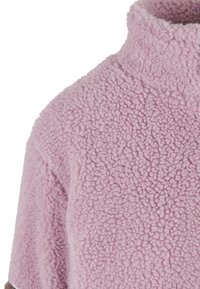 Suéter de forro polar rosa claro con cuello alto, que presenta una superficie texturada y esponjosa y manga corta. Diseño simple, sin hardware visible.