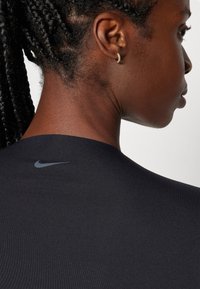 Mustmustrihane mustshirt mustrihasega, sujuv ja veniv tekstuuriga, mille ülaservas asub väike hall Nike logo, rõhutades minimalistlikku disaini.