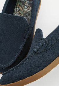 Mørkeblå ruskinds loafers med en mokkasin-design, der har syede detaljer og en brunt gummisål, velegnet til afslappet brug.