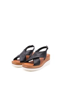 Sandali in pelle nera con cinturini incrociati, soletta in pelle marrone e suola a zeppa bianca. Cinturino alla caviglia regolabile per una vestibilità sicura.
