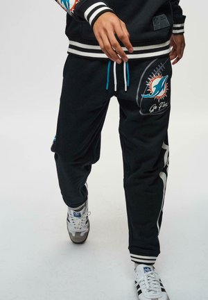 Zwarte trainingsbroek met blauwe koordjes, voorzien van het logo van de Miami Dolphins en de tekst "Go Fins". Gestreepte boorden en zijkanten zorgen voor een betere uitstraling.