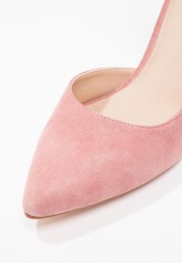 Rosa mocka högklackad sko med spetsig tå och lågskuren design som avslöjar det inre fodret och den texturerade ytan.