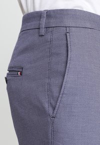 Pantaloni a motivi blu navy con una trama testurizzata, dotati di una tasca laterale e un piccolo accento del marchio vicino alla tasca. Vestibilità sartoriale.