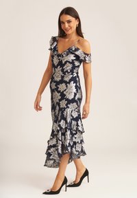 Navy dress with silver floral pattern, ruffled neckline and hem, fitted silhouette, paired with black heels featuring a decorative accent.