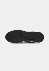 Suola di scarpa in gomma nera con un disegno di battistrada dettagliato, caratterizzata da una soletta bianca e da rifiniture marroni. Il nome del marchio "GUESS" è visibile sulla suola.