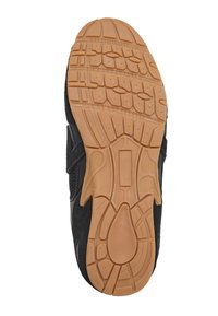 Semelle noire de chaussure de sport avec une bande en caoutchouc beige présentant une adhérence à motif et le nom de la marque embossé au centre.