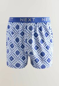 Mėlynos ir baltos spalvos šortai su geometriniais raštais, elastinga juosta su "NEXT" ženklu ir priekiniu mygtuku.