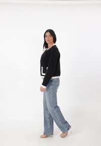 Suéter negro corto con ribete crema y detalle de bolsillo, combinado con jeans de mezclilla holgados y sandalias de tacón transparente. Fondo blanco.