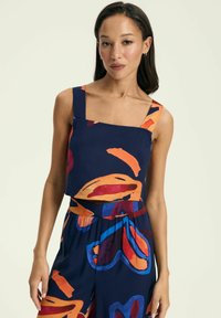 Granatowy krótki top z szerokimi ramiączkami, z wyrazistymi pomarańczowymi i niebieskimi abstrakcyjnymi wzorami. Gładka tekstura materiału, dopasowany krój i kwadratowy dekolt.